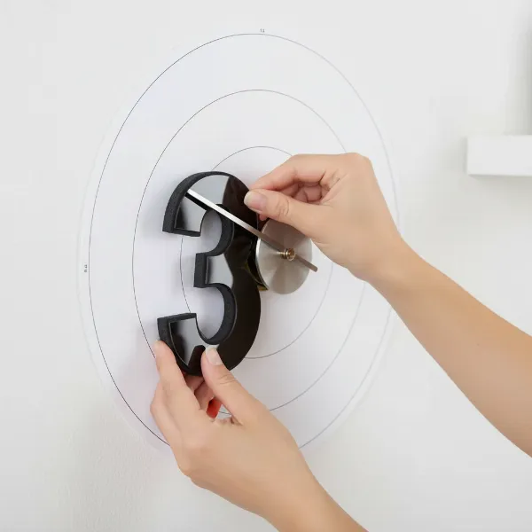 A person installing the self-adhesive numbers of a 3D frameless DIY wall clock using a template.