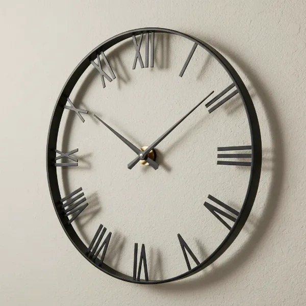 Infinity Instruments The Tower Wall Clock with sleek black metal frame and Roman numerals on a light wall.